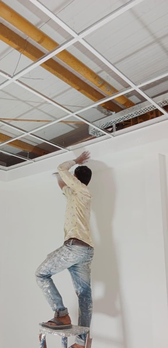 Worker on a ladder fixing a grid ceiling.