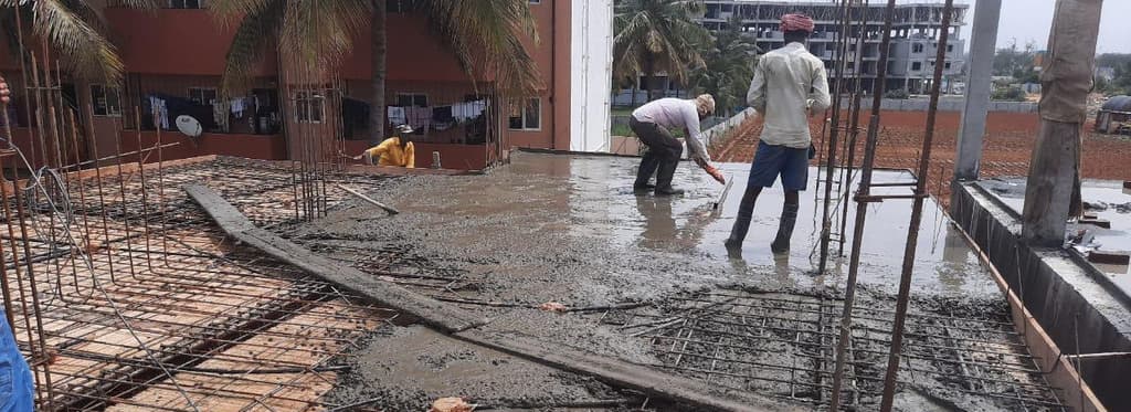 Workers levelling freshly poured concrete on a roof slab.
