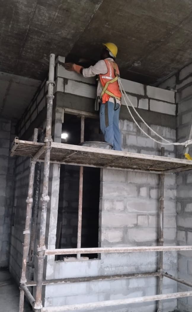 Mason laying blocks from scaffolding beside a door opening.