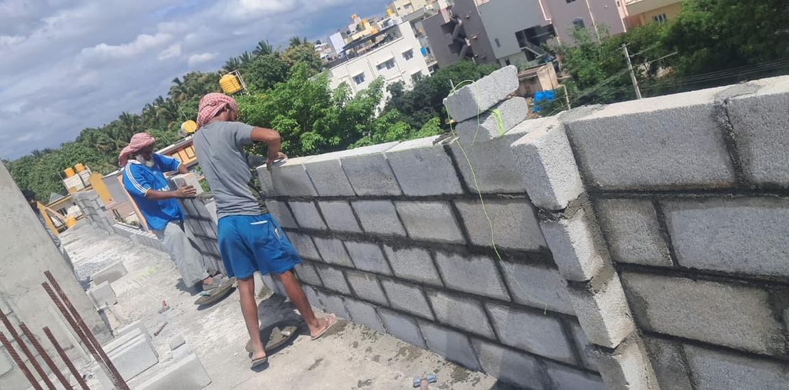 Masons laying concrete blocks on a wall at roof level.