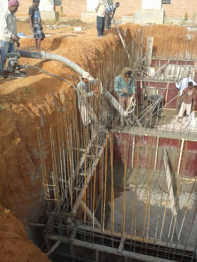Workers concreting tank walls inside the excavation.