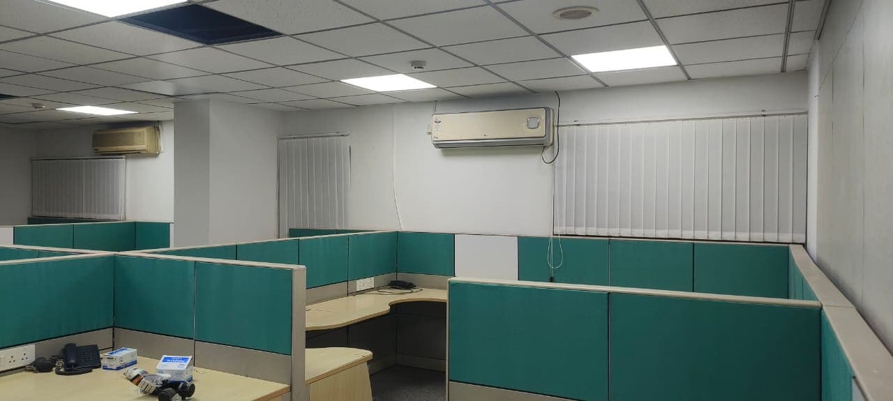 Office with teal workstation partitions under a grid ceiling.