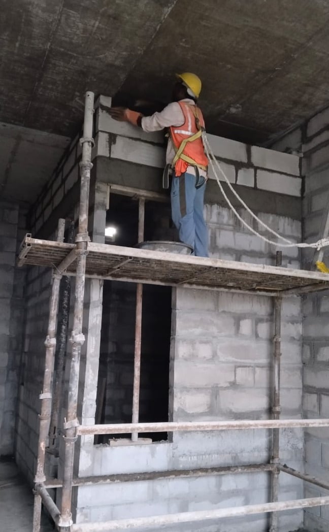 Mason laying blocks from scaffolding beside a door opening.